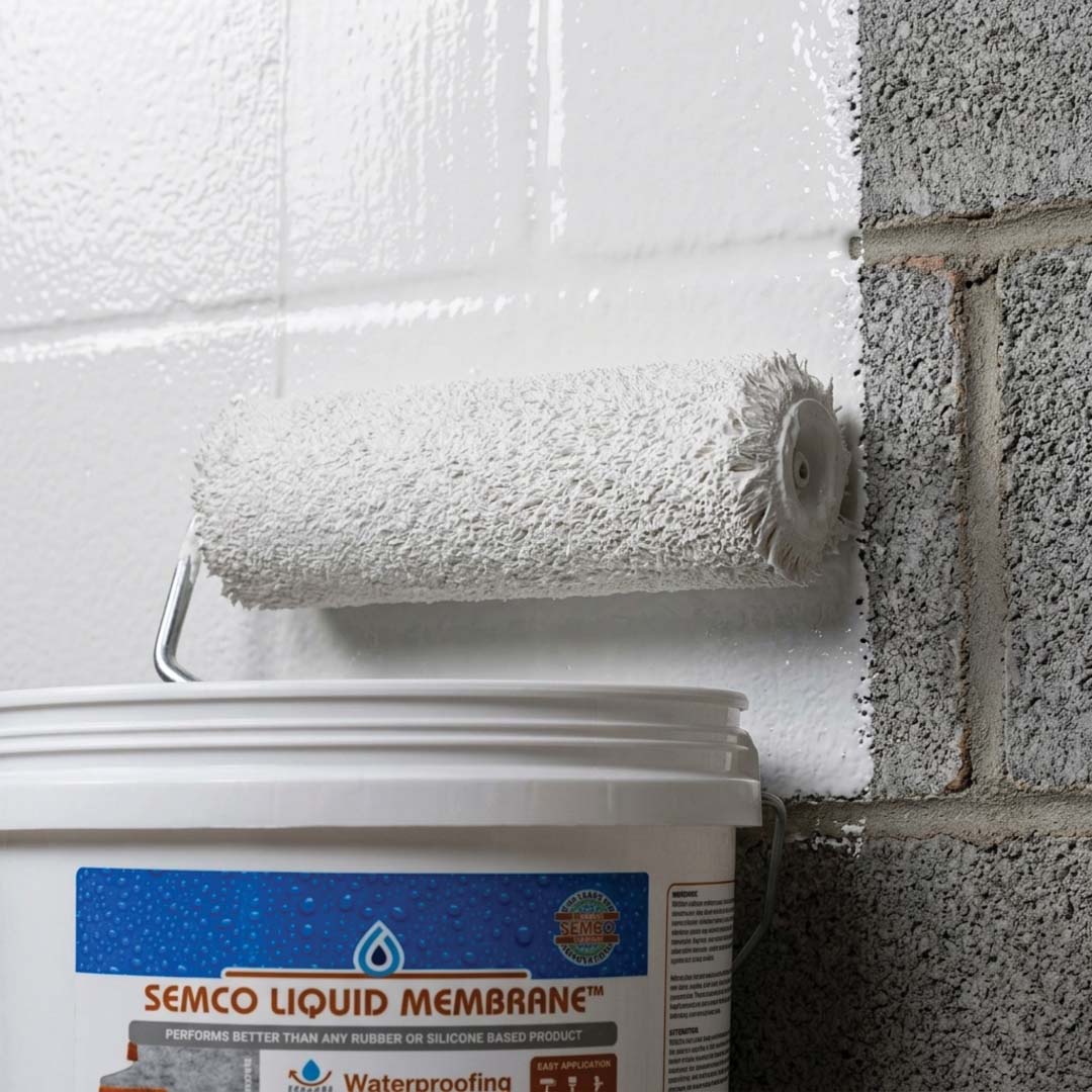 Close-up of a roller applying a smooth white waterproofing membrane coat over a grey cinder block basement wall